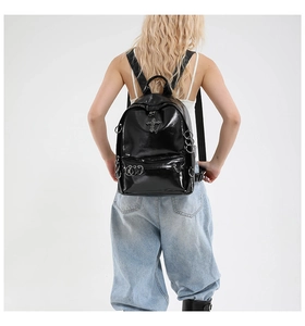 Detail of glossy black gothic backpack featuring metal cross and silver ring piercings