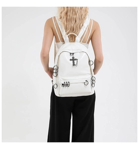 Detailed view of white punk style backpack with cross pendant and metal ring ornaments