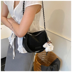 Détail d'un sac bandoulière en cuir noir avec chaîne argentée et pendentif chiot