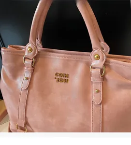 Detail einer rosa Kunstledertasche mit goldener Hardware und Metall-Logo-Plakette