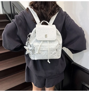 Detailed back view of white backpack with star patterns and silver charms on a model