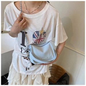 Sac à bandoulière bleu clair avec chaîne et breloque en peluche porté par un modèle