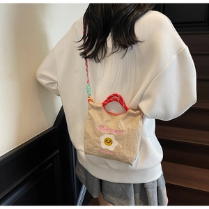 Dettaglio borsa in tela con ricamo uovo fritto e tracolla arcobaleno colorata su modella