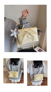 Detail of a creamy yellow shoulder bag with a shiny bow, silver chain, and star charm