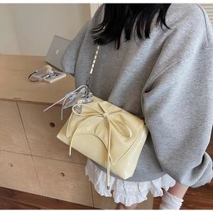 Detail of pale yellow ballet-style bow shoulder bag with silver star charm and chain strap