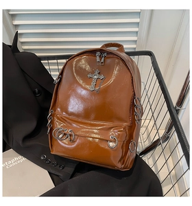 Detailed view of punk style brown patent leather backpack with metal cross and chains