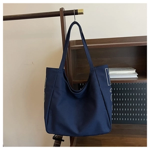 Close-up of a large navy blue canvas tote bag with letter print hanging on a hanger