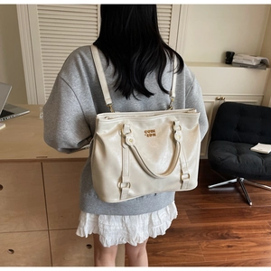Detail der cremefarbenen Tragetasche mit Goldlogo und Backpack-Konvertierung