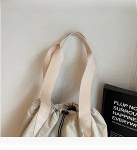 Detail of reinforced wide handles and drawstring closure on the beige nylon backpack