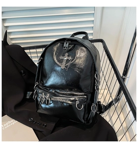 Detail of glossy black punk backpack featuring a silver gothic cross and chain accents