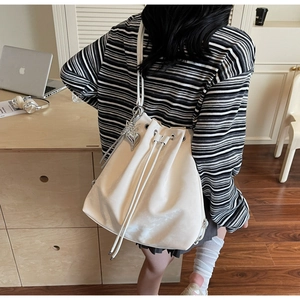 Detail showing white drawstring bucket bag with silver heart charm on model back