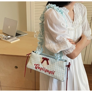 Detail of blue plaid underarm bag with red bow and ruffled strap on white lace dress