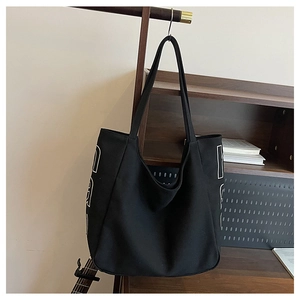 Detail of a large black canvas tote bag with white letter design hanging in a casual setting