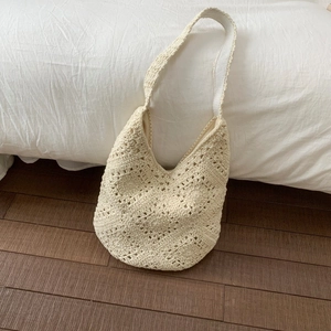 Close-up of beige woven hobo bag with bohemian cutout floral patterns and wide strap