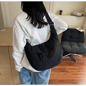 Detail view of large black nylon dumpling bag with adjustable wide strap and side woven label