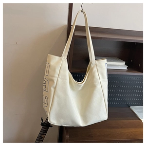 Close-up of beige canvas tote bag with blue letter print hanging on a bookshelf