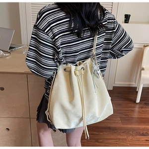 Shoulder shot of a cream drawstring bucket bag with silver butterfly charms in a minimalist room
