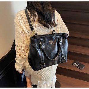 Detailaufnahme der schwarzen Ledershopper-Tasche mit Goldbeschlägen auf einer Treppe