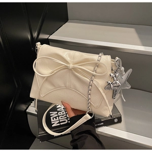 Close-up of beige leather shoulder bag featuring a large bow and silver chain with charms