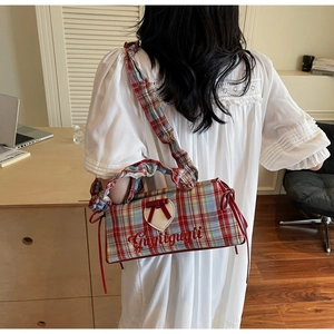 Detail of red and blue plaid crossbody bag featuring heart patch and bow on white dress