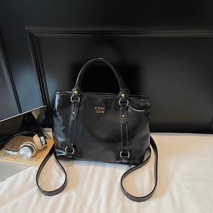 Detail der glänzenden schwarzen Lackledertasche mit goldenem Logo und verstellbarem Gurt
