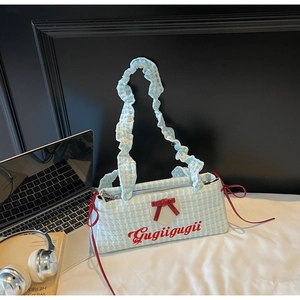 Close-up of blue plaid handbag with red bow detail and ruffled handle on desk