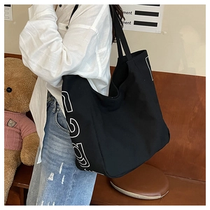 Detail of a large black canvas tote bag with white lettering in a cozy lifestyle setting