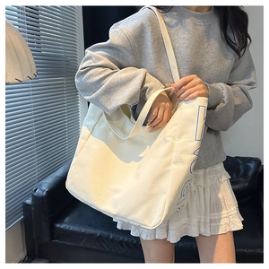 Detailed shot of large white canvas tote bag with blue text worn by a model in casual style