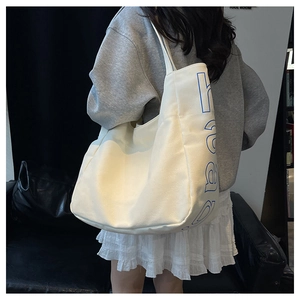 On-shoulder view of large white canvas tote bag with blue heart lettering for women