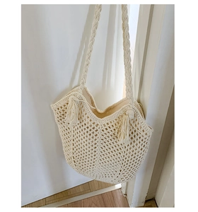Detail of hand-woven hollow mesh tote bag with bohemian tassels and braided handles