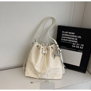 Detail of cream drawstring bucket bag featuring a silver butterfly heart pendant charm