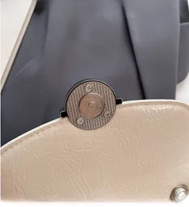 Vue détaillée du fermoir magnétique en métal argenté sur un sac à main blanc cassé