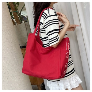 Detail of red canvas tote bag with white letter print worn by a model in casual setting