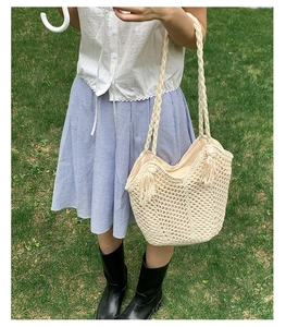 Detail of off-white woven tote with hollow mesh texture and tassels on green grass