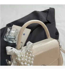 Détail du sac à main crème texture crocodile avec nœud en dentelle de perles et poignée