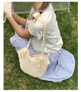 Close-up of beige woven tote bag with hollow mesh design and tassel detail on grass