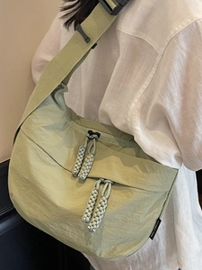 Pale green dumpling-style nylon crossbody bag with adjustable wide strap and woven zippers