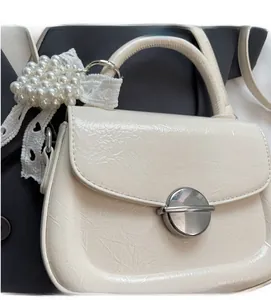 Gros plan d'un sac en cuir texturé crème avec grappes de perles et ruban en dentelle