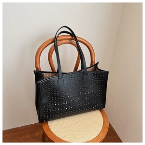 Détail d'un sac cabas noir avec motif circulaire ajouré posé sur une chaise en rotin