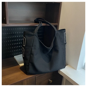 Close-up of a black canvas tote bag with white letter design on a dark bookshelf
