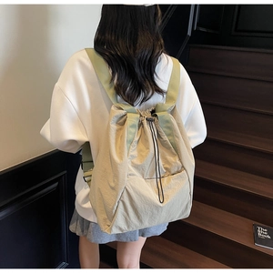 Detail view of beige drawstring backpack with green straps and wrinkled nylon texture