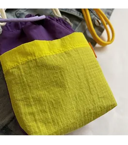Detail of color-block drawstring bag showing purple nylon fabric and yellow plaid pocket
