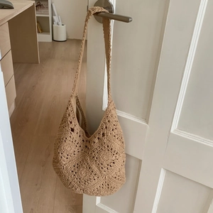 Detail of floral hollow crochet weave on beige hobo shoulder bag hanging on a white door