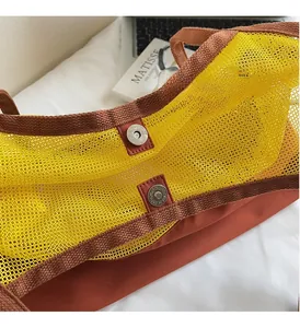 Detail of the metal magnetic snap closure on yellow mesh tote bag with rust-red straps