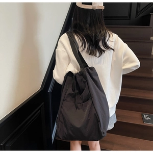 Lifestyle view of a black drawstring nylon tote bag worn by a model on a wooden staircase