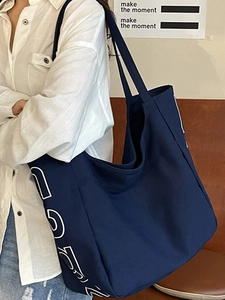 Large navy blue canvas tote bag with white lettering, shown on model in a casual setting