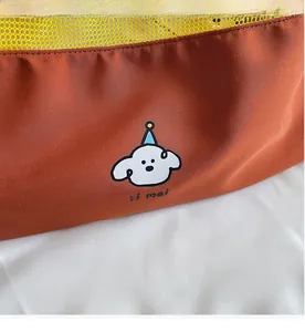 Detail of a brown nylon tote bag with yellow mesh stitching and cartoon dog illustration