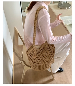 Detailed macro view of woven straw tote bag with tassel charms and thick braided shoulder strap