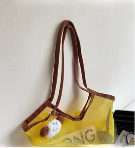 Detail of yellow mesh tote bag with brown woven handles and white plush puppy charm