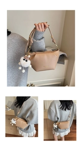 Detail of khaki leather dumpling bag with gold logo and fluffy monster keychain accessory